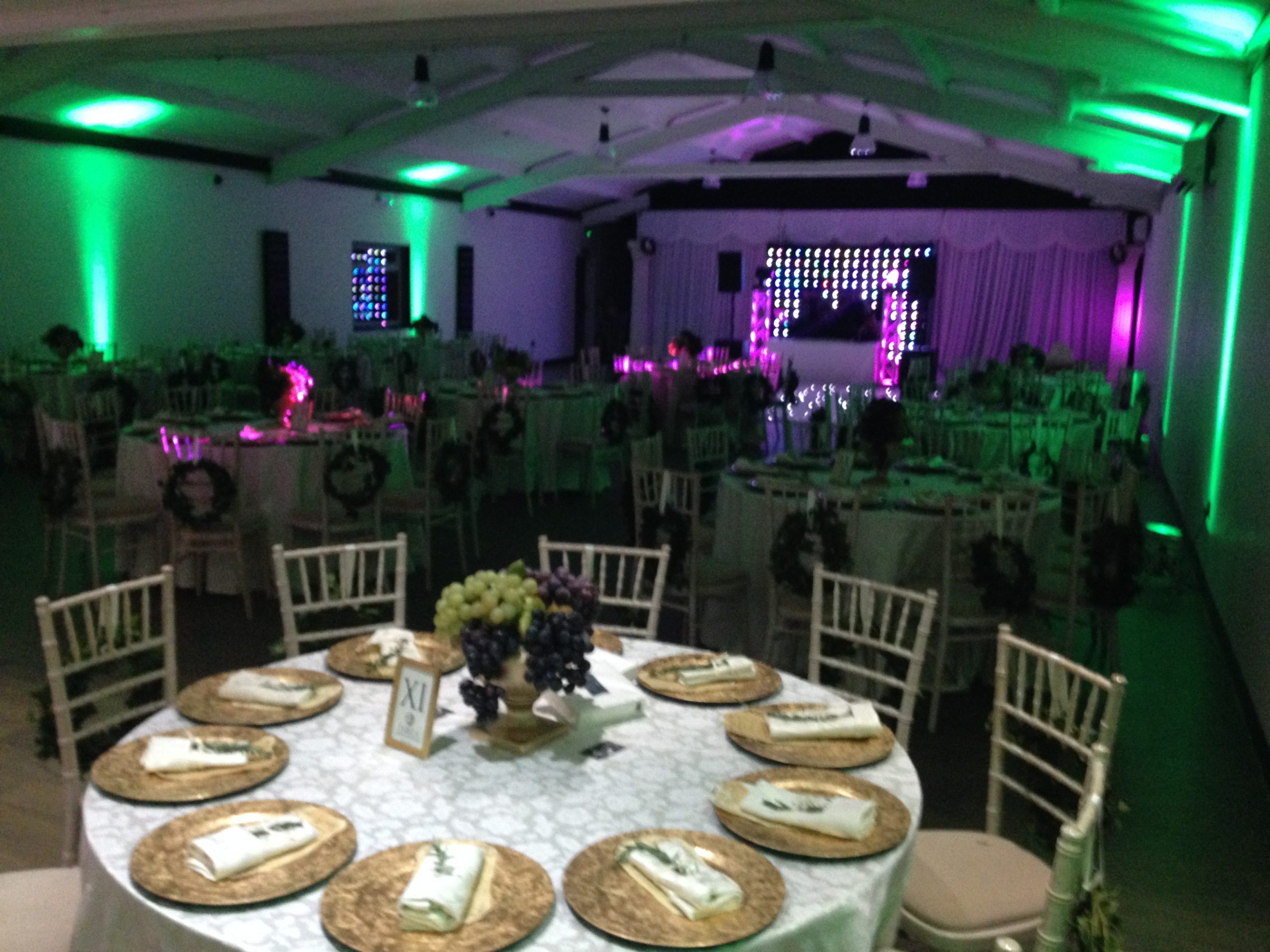 Round tables with gold chargers and festive centrepieces under green uplighting.