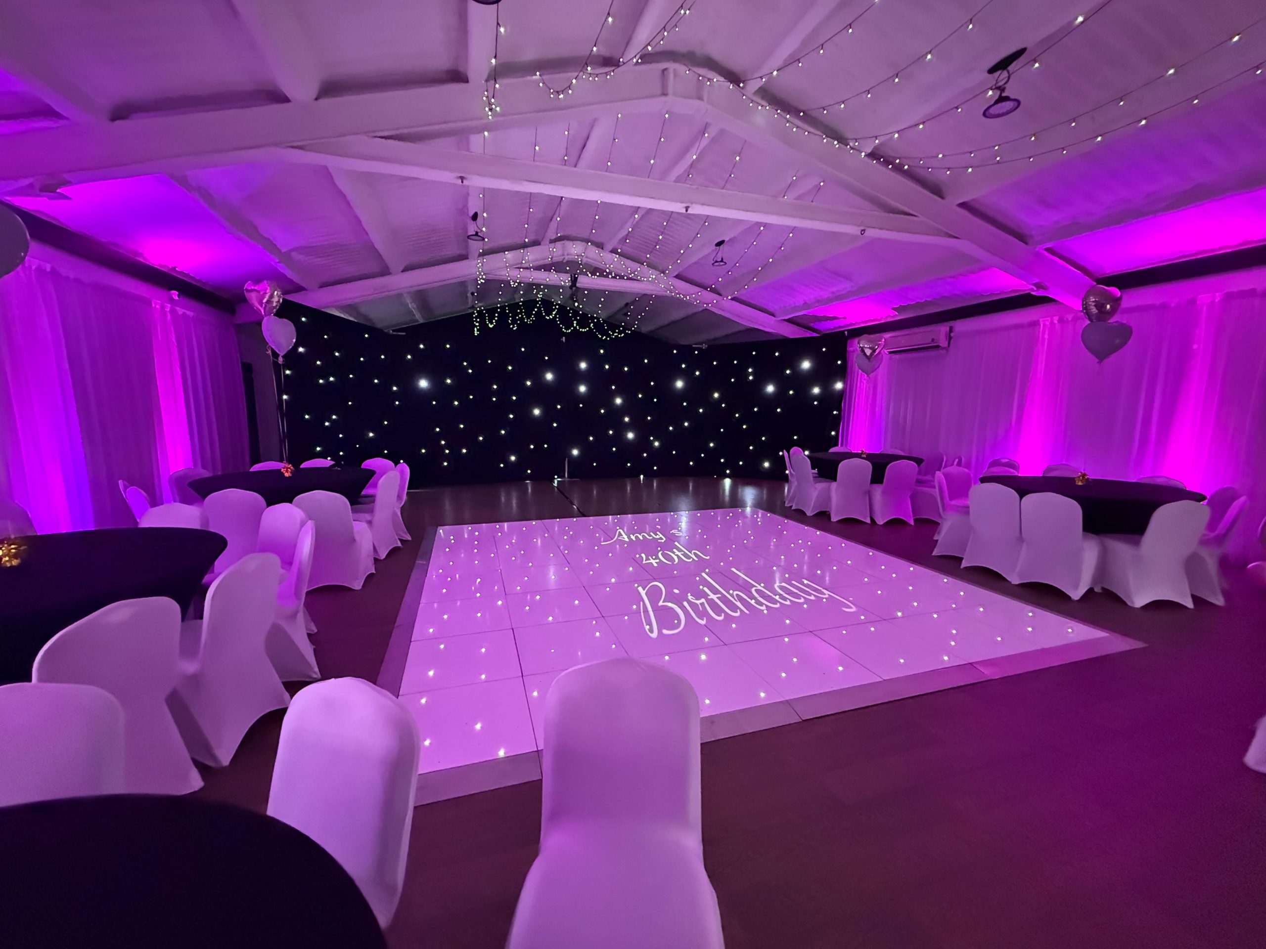 The hall at Venue 92 with a starlit LED dance floor, white chair covers and pink uplighting.