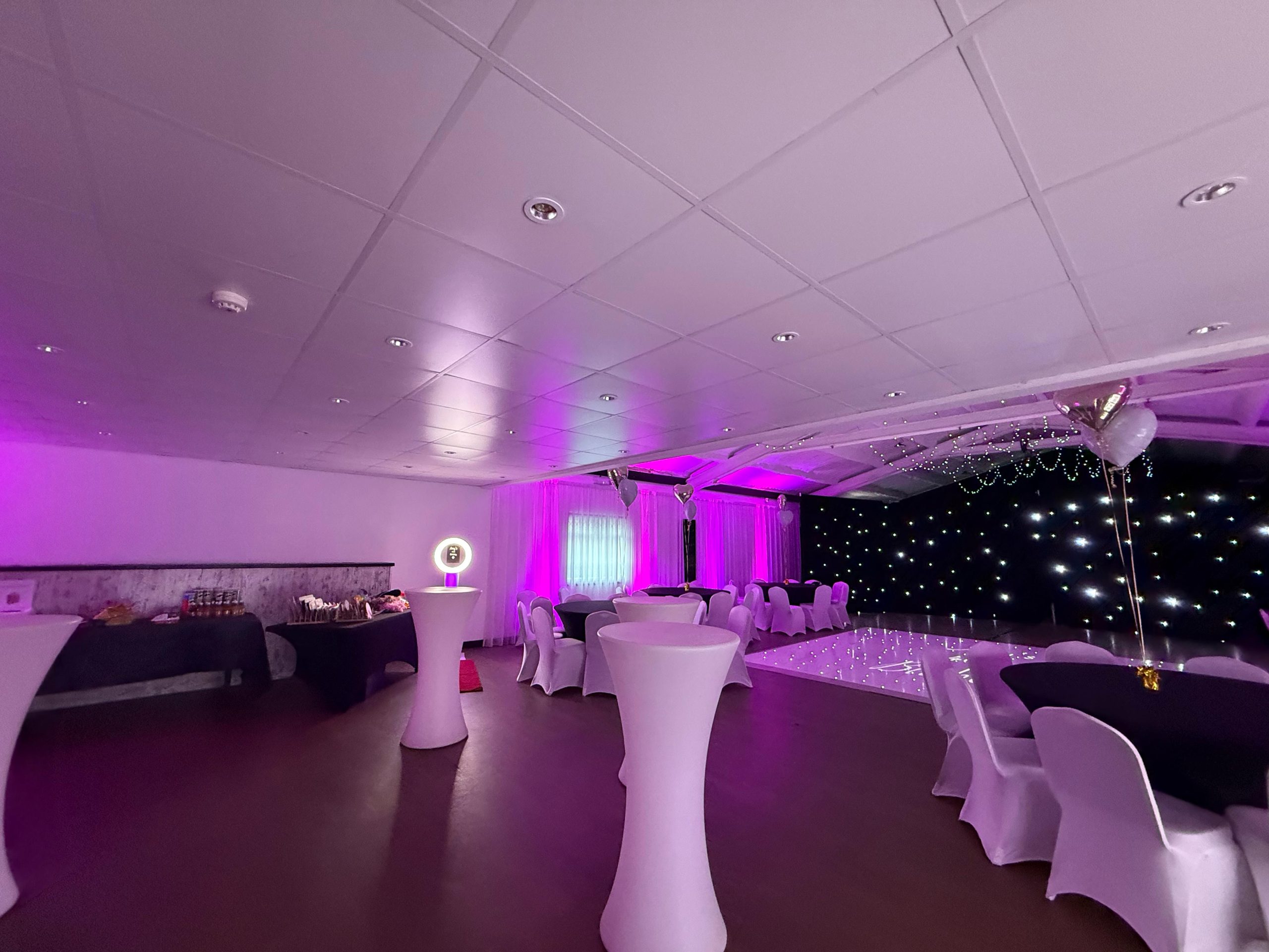 Poseur tables and dressed round tables in front of a starlit backdrop in the hall.