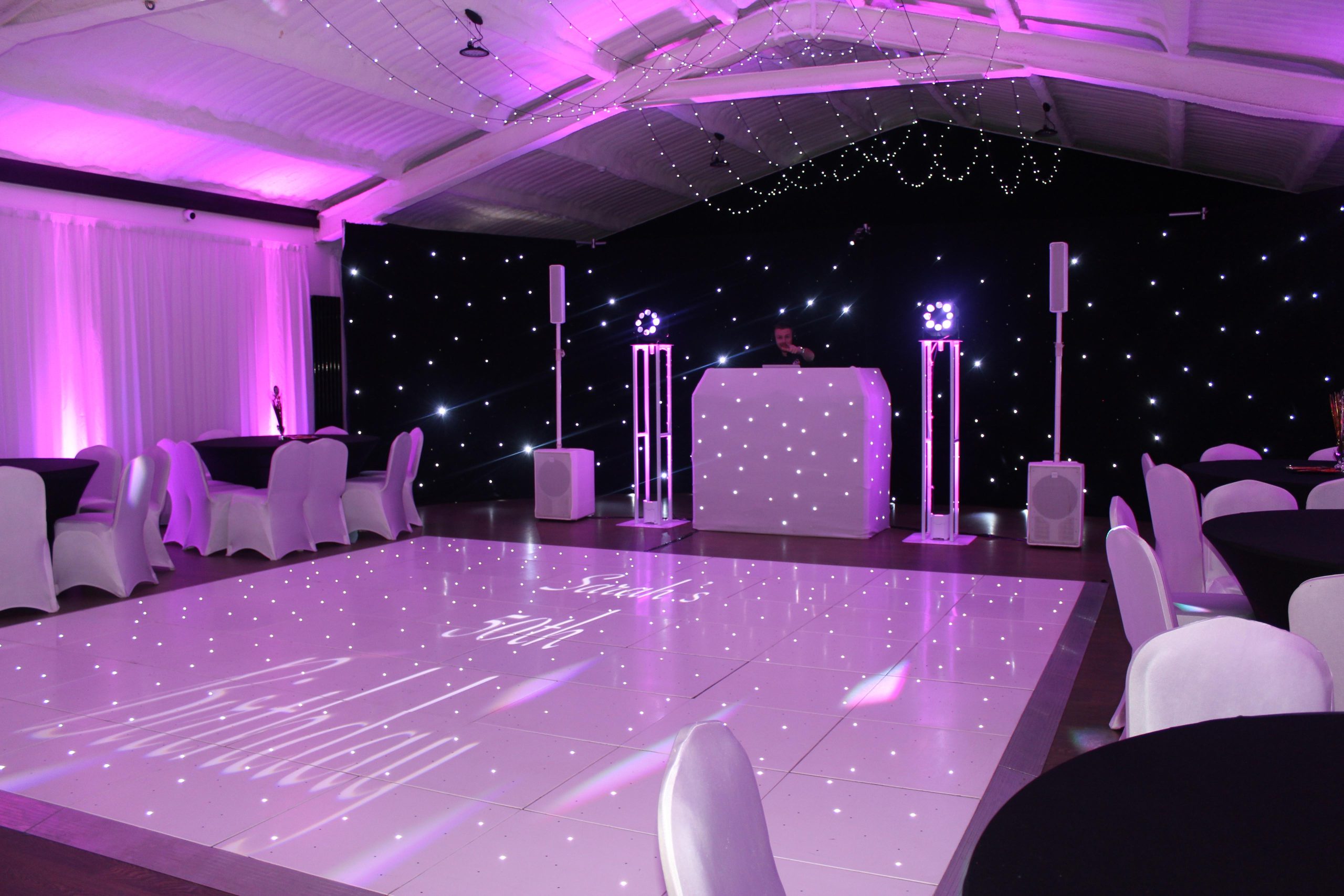 A white LED dance floor and DJ booth in front of a starlit backdrop.